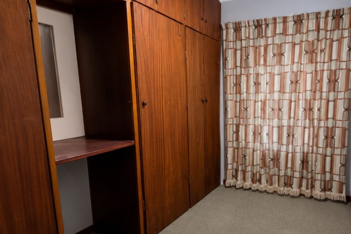 A bedroom featuring extensive floor-to-ceiling built-in wooden cabinetry, neutral carpeting, and a window with curtains.