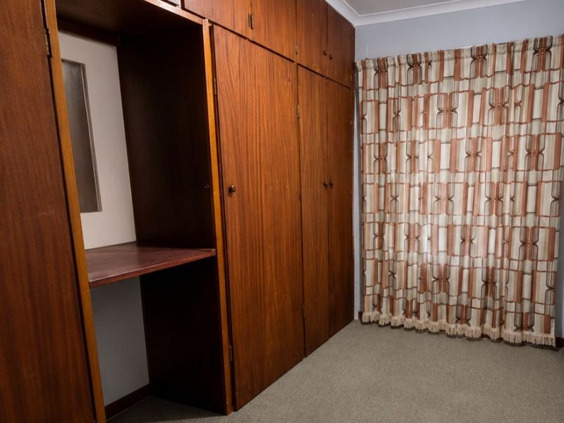 A bedroom featuring extensive floor-to-ceiling built-in wooden cabinetry, neutral carpeting, and a window with curtains.