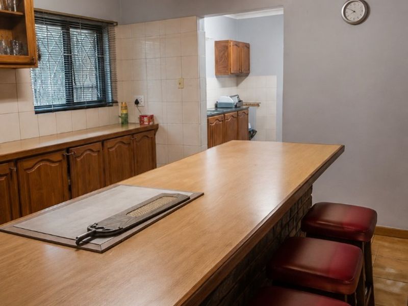 A functional kitchen featuring a breakfast bar, timber ceiling, tiled splashbacks, and a connected scullery area with additional cabinetry.