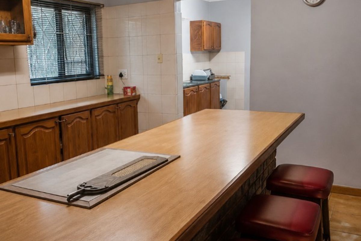 A functional kitchen featuring a breakfast bar, timber ceiling, tiled splashbacks, and a connected scullery area with additional cabinetry.