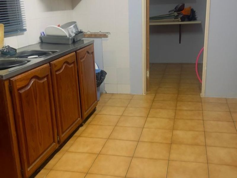 A functional scullery area featuring built-in wooden cabinetry, a stainless steel sink, tiled flooring, and an adjoining pantry space.