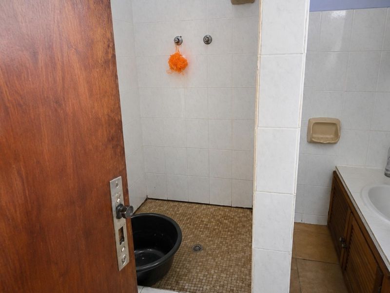 A functional bathroom featuring a tiled shower enclosure, vanity cabinet with integrated sink, and dated wall and floor tiling.