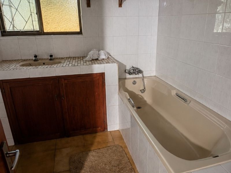 A dated bathroom featuring a built-in bathtub, tiled vanity with storage, and timber ceiling, offering potential for a modern renovation.