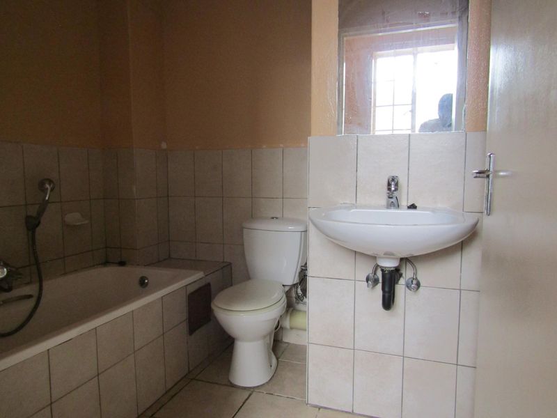 A functional bathroom featuring a bathtub, toilet, and wall-mounted basin with tiled finishes, requiring cosmetic updates to improve its overall aesthetic appeal.