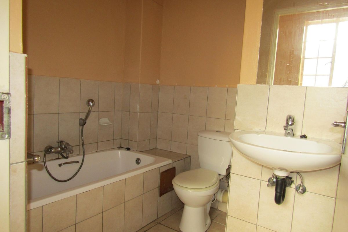 A functional bathroom featuring a bathtub with handheld shower, toilet, and wall-mounted basin, requiring cosmetic updates to improve its dated appearance.