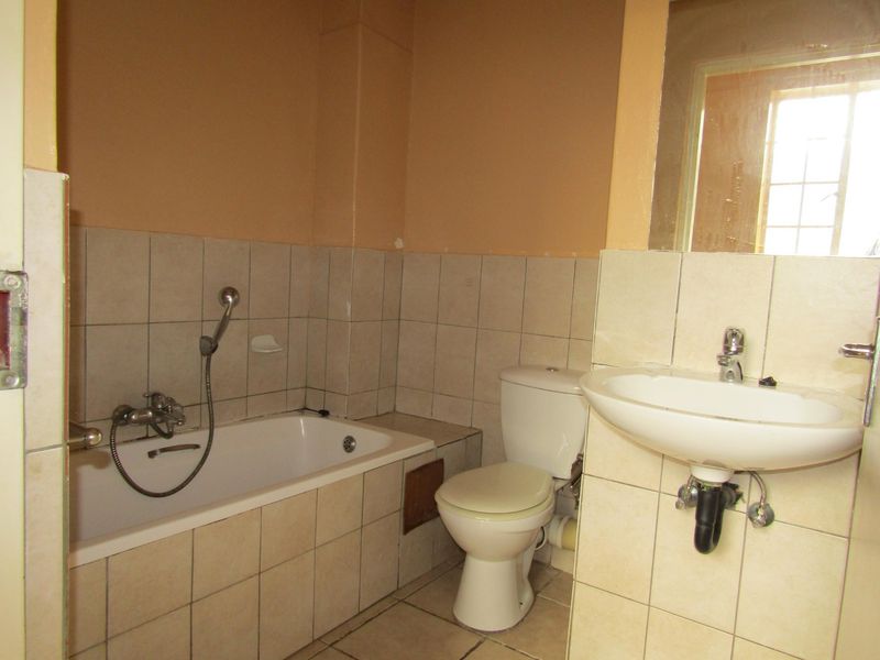 A functional bathroom featuring a bathtub with handheld shower, toilet, and wall-mounted basin, requiring cosmetic updates to improve its dated appearance.