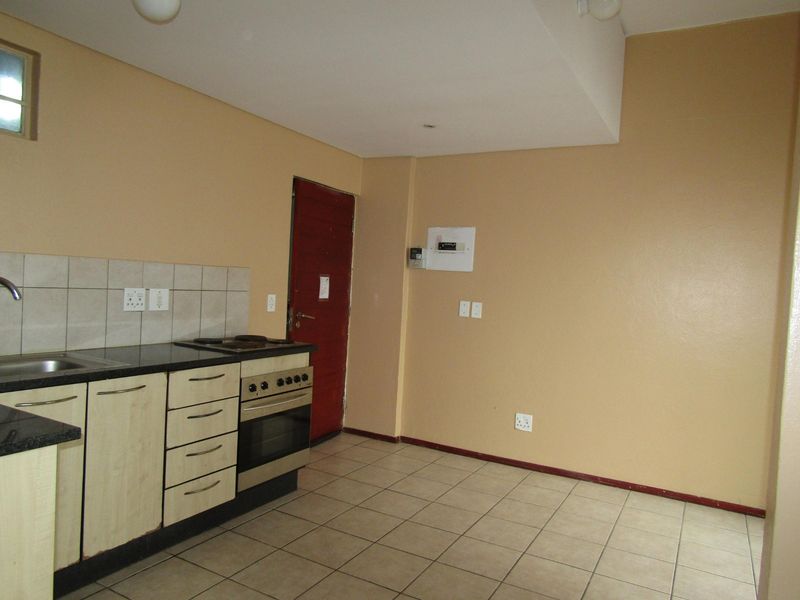 A functional kitchen featuring built-in cabinetry, laminate countertops, a tiled splashback, and a freestanding oven, with neutral wall tones and tiled flooring throughout.