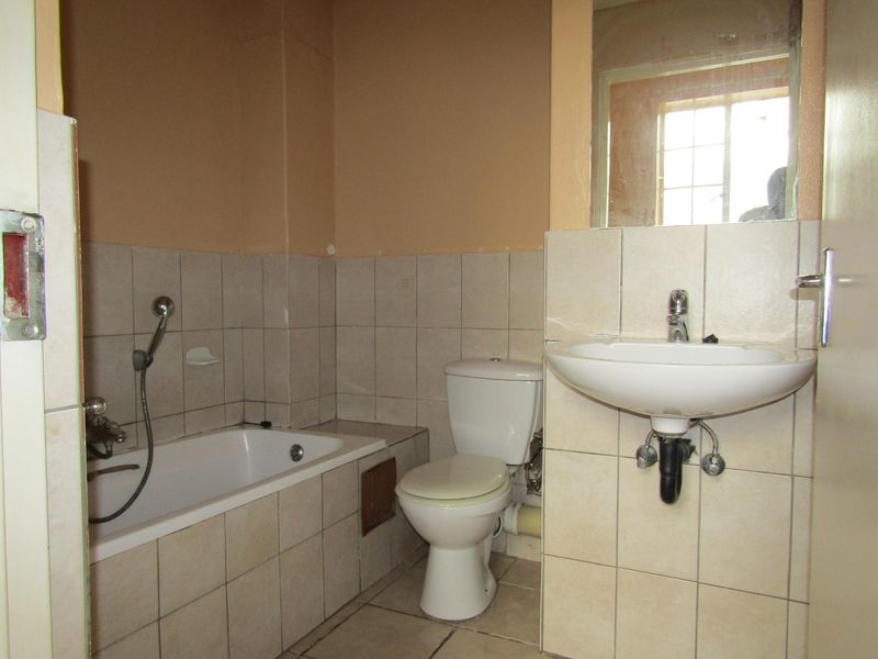 A functional bathroom featuring a bathtub with handheld shower, toilet, and pedestal washbasin, finished with neutral wall and floor tiles.