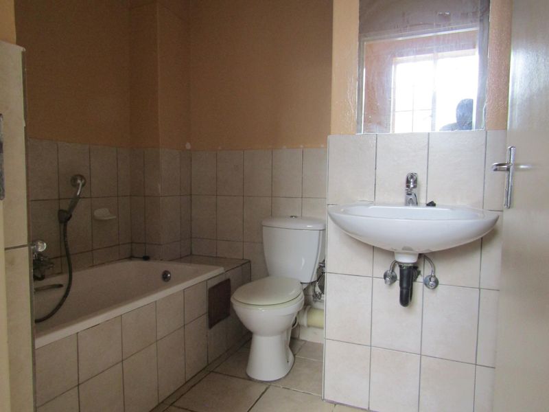 A functional bathroom featuring a bathtub, toilet, and wall-mounted basin with tiled finishes, requiring some cosmetic updates to improve its overall condition.