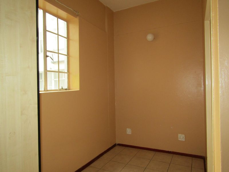 An empty bedroom featuring tiled flooring, a built-in cupboard, and a window with security bars, providing a blank canvas for personalization.