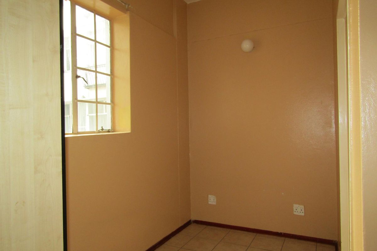 An empty bedroom featuring tiled flooring, a built-in cupboard, and a window with security bars, providing a blank canvas for personalization.
