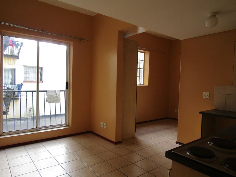 An empty open-plan living and kitchen area featuring tiled floors, a sliding door to a balcony, and basic built-in kitchen cabinetry.