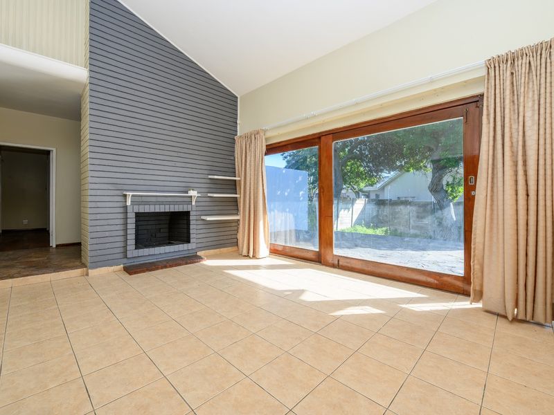 Spacious living room featuring a vaulted ceiling, a fireplace with a grey brick feature wall, and large sliding glass doors opening to the garden.