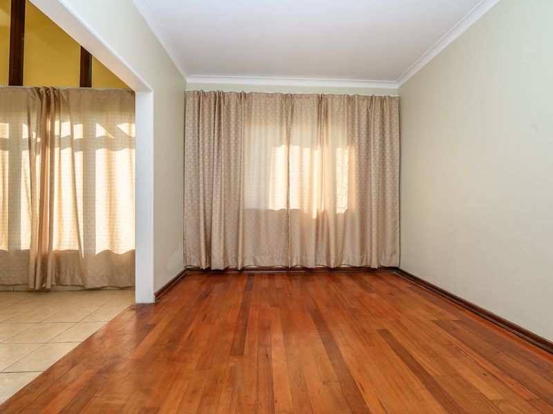 An empty living room featuring polished hardwood flooring, neutral wall tones, and a seamless transition to an adjacent tiled area.