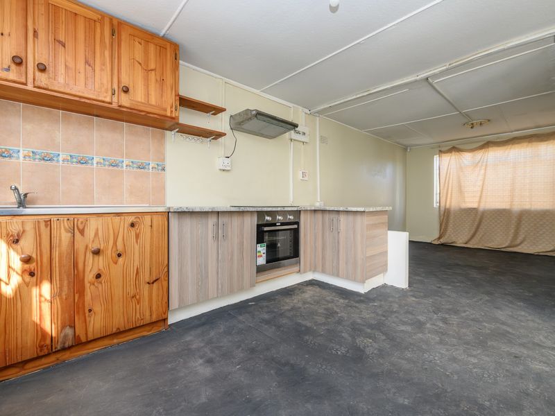 Open plan kitchen and living area featuring dated wooden cabinetry, built-in oven, and exposed ceiling panels, offering significant potential for renovation and modernization.