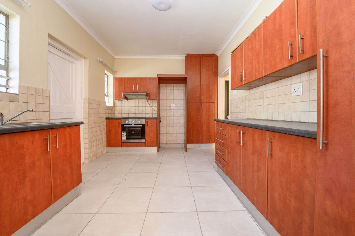 A functional, empty kitchen featuring wood-finish cabinetry, tiled backsplash, built-in oven with extractor fan, and neutral ceramic floor tiles.