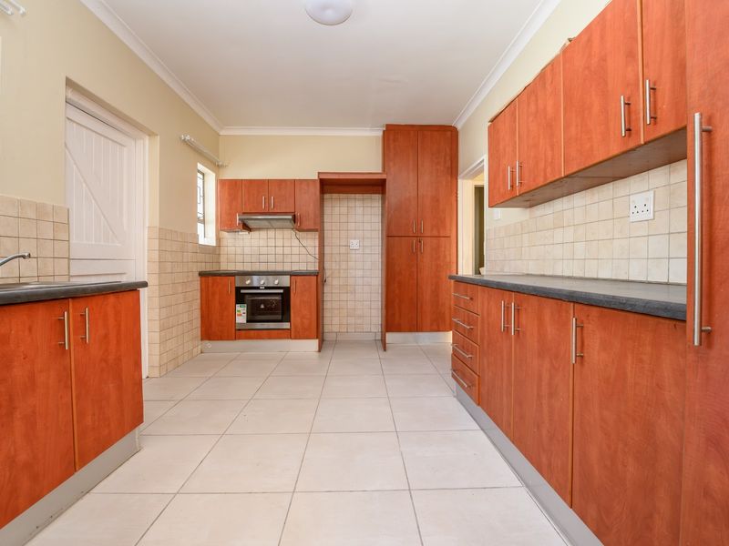 A functional, empty kitchen featuring wood-finish cabinetry, tiled backsplash, built-in oven with extractor fan, and neutral ceramic floor tiles.