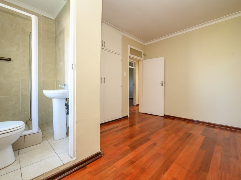 A spacious bedroom featuring hardwood flooring, built-in cupboards, and an attached en-suite bathroom with a shower, basin, and toilet.