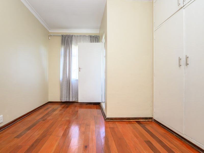 A bright, empty bedroom featuring polished hardwood flooring, built-in storage cupboards, and neutral wall finishes.