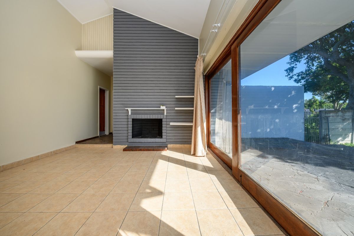 Spacious living area featuring a vaulted ceiling, a central fireplace with a grey feature wall, and large sliding glass doors opening to the exterior.