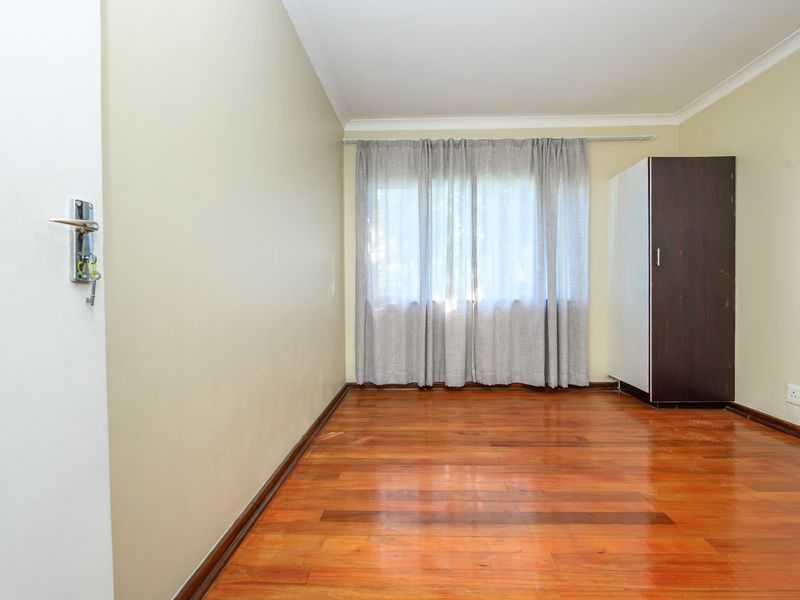 A bright, empty bedroom featuring polished hardwood flooring, neutral wall tones, and a window with curtain tracks.