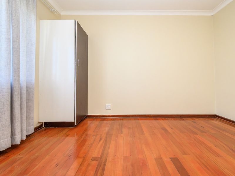 A bright, empty bedroom featuring polished hardwood flooring, neutral walls, and a built-in cupboard, offering a clean and versatile living space.