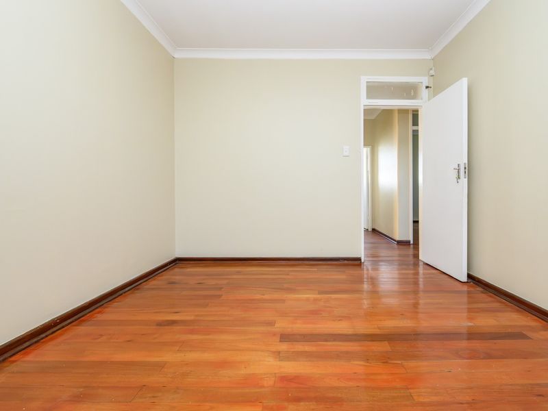 A bright, empty bedroom featuring polished hardwood flooring, neutral walls, and a classic internal door with a transom window.