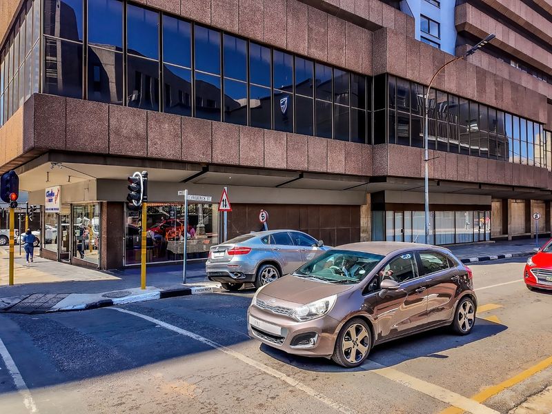 Street-level view of a commercial building featuring a brown concrete facade and extensive glass curtain walling at a busy urban intersection.