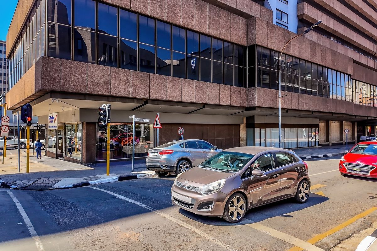 Street-level view of a commercial building featuring a brown concrete facade and extensive glass curtain walling at a busy urban intersection.