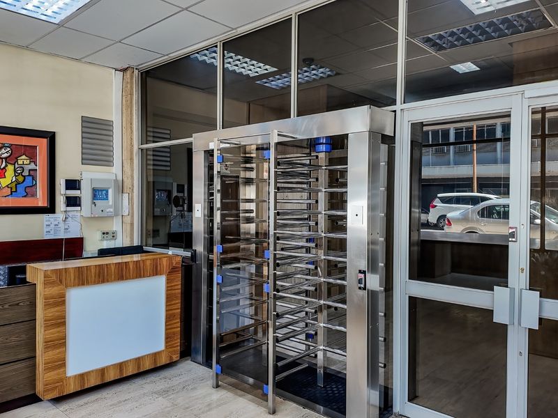 Commercial building entrance featuring a stainless steel security turnstile, reception desk, and glass partition wall with integrated security systems.