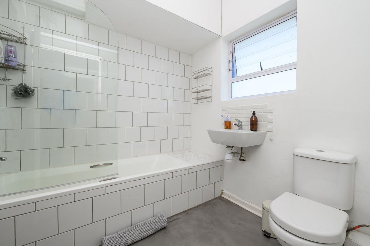 A functional bathroom featuring a bathtub with a glass screen, wall-mounted basin, and toilet, finished with white subway tiling.