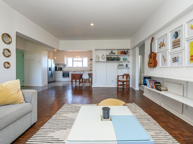 Spacious open-plan living and kitchen area featuring warm parquet flooring, built-in wall shelving, and a functional kitchen with integrated appliances.