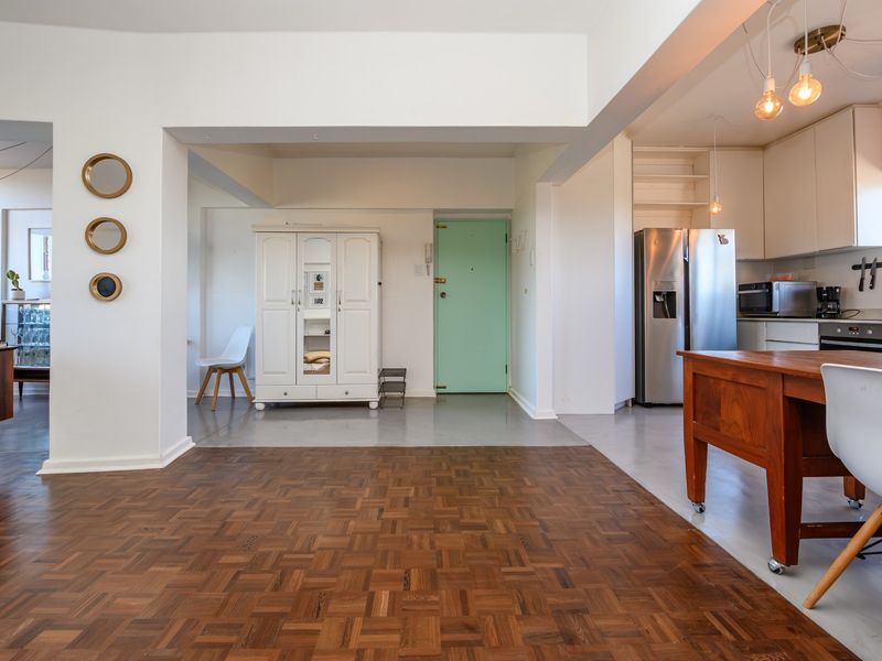 Spacious open-plan living area featuring a blend of classic parquet and modern polished concrete flooring, seamlessly connected to a functional kitchen space.
