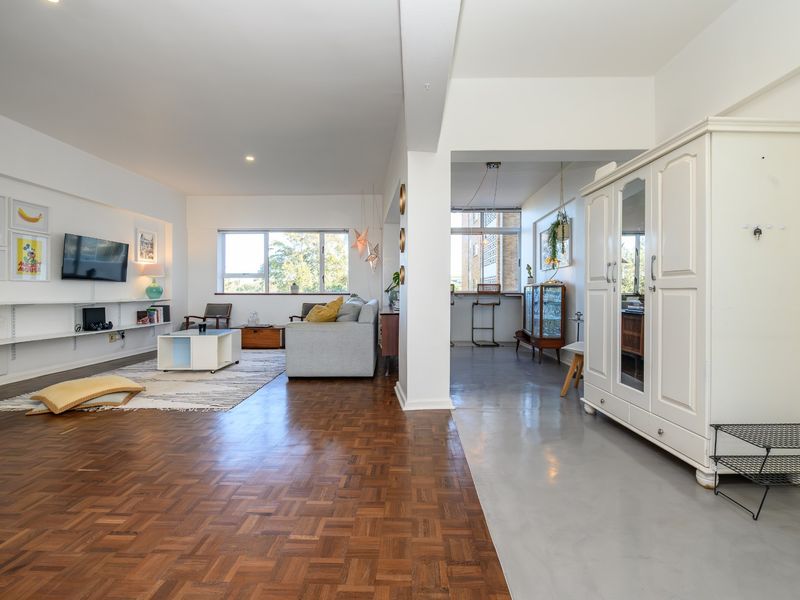 Spacious open-plan living area featuring a blend of classic parquet and modern polished concrete flooring with integrated shelving and ample natural light.