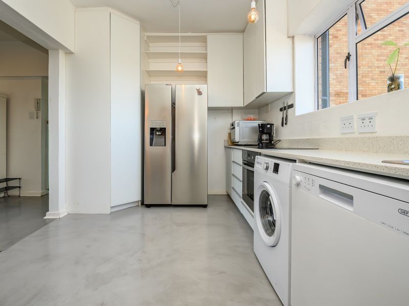 A functional kitchen featuring white cabinetry, stone countertops, integrated appliances, and polished concrete flooring, offering a clean and modern aesthetic.