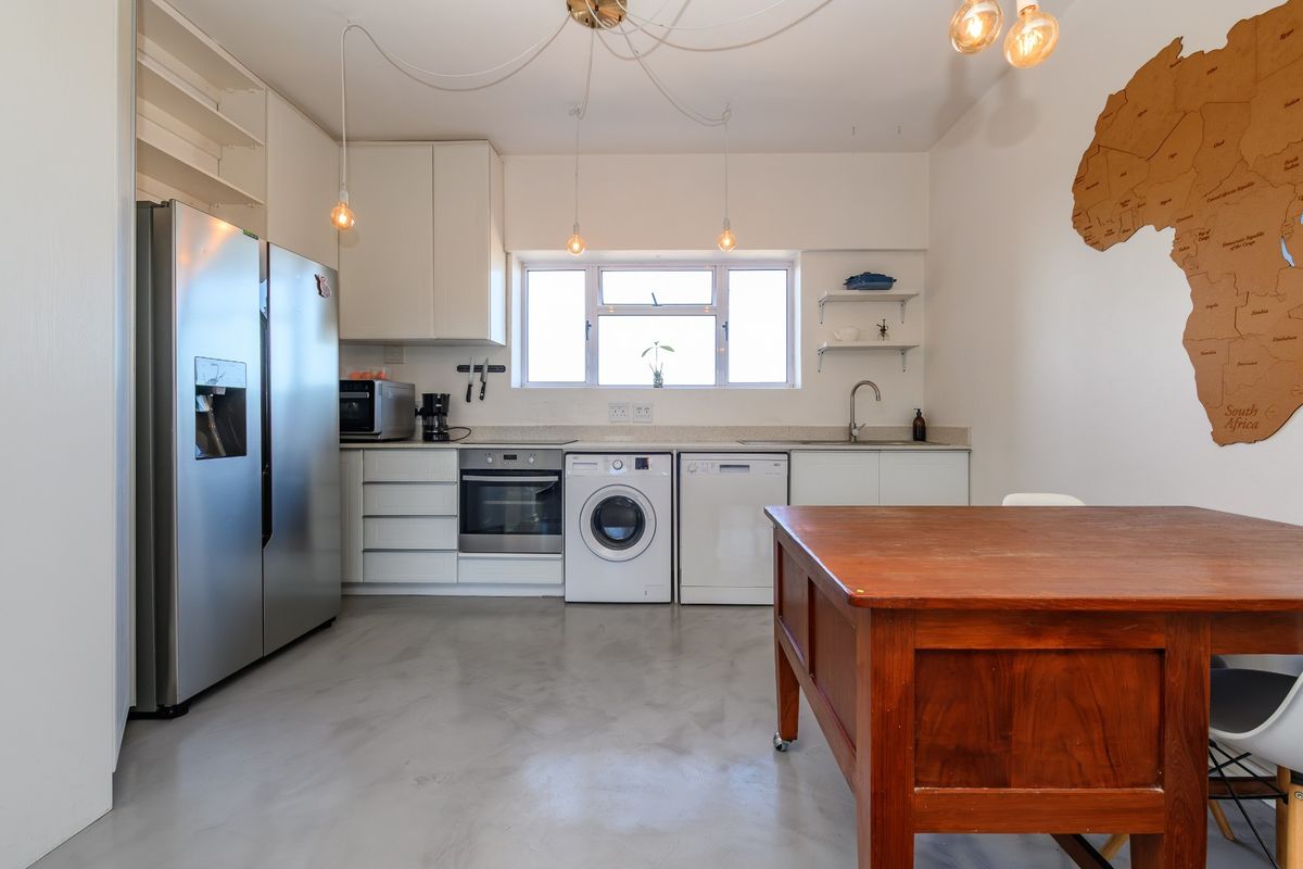 A modern kitchen featuring white cabinetry, polished concrete floors, built-in oven, and integrated laundry appliances, offering a clean and functional workspace.