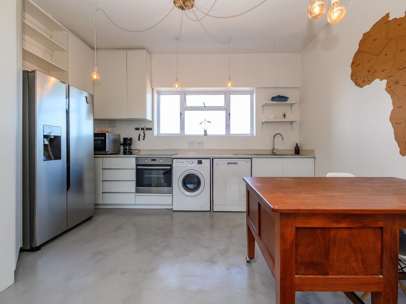 A modern kitchen featuring white cabinetry, polished concrete floors, built-in oven, and integrated laundry appliances, offering a clean and functional workspace.