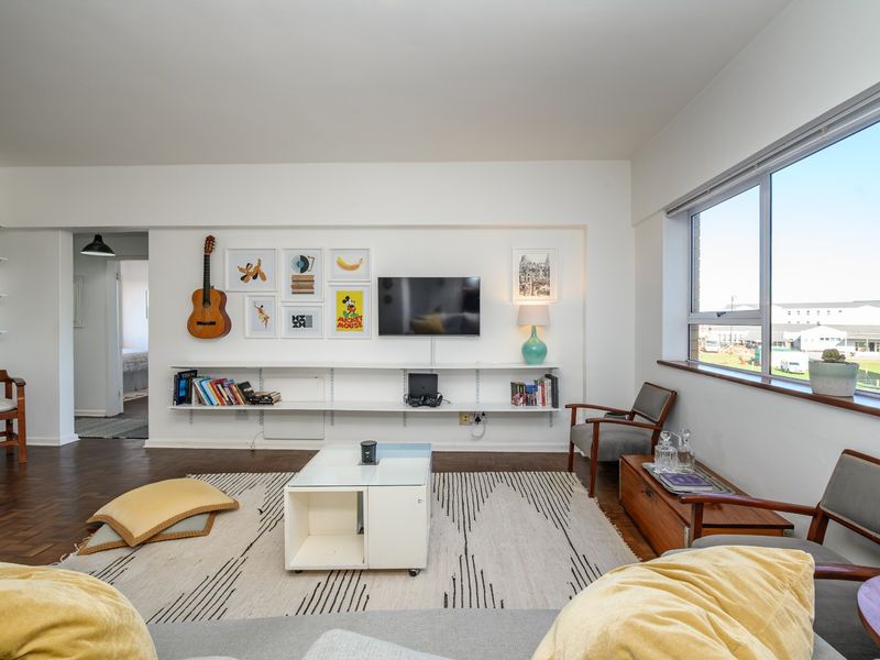 A bright living room featuring parquet flooring, built-in wall shelving, and a large window providing natural light and an exterior view.