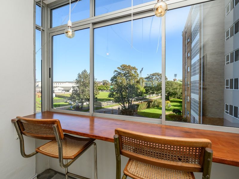 Enclosed balcony area featuring a built-in wooden breakfast bar and large windows offering pleasant views of the surrounding neighborhood and green space.