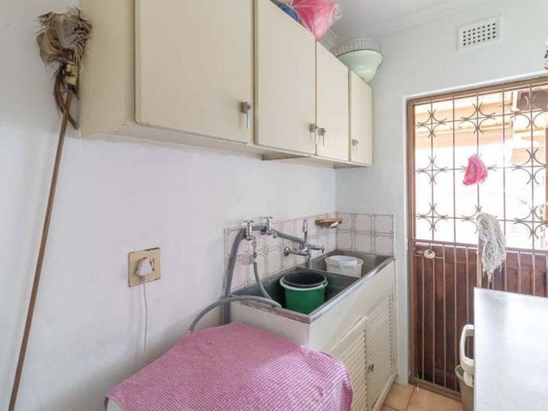A functional laundry area featuring built-in cabinetry, a utility sink, and a security gate leading to the exterior.