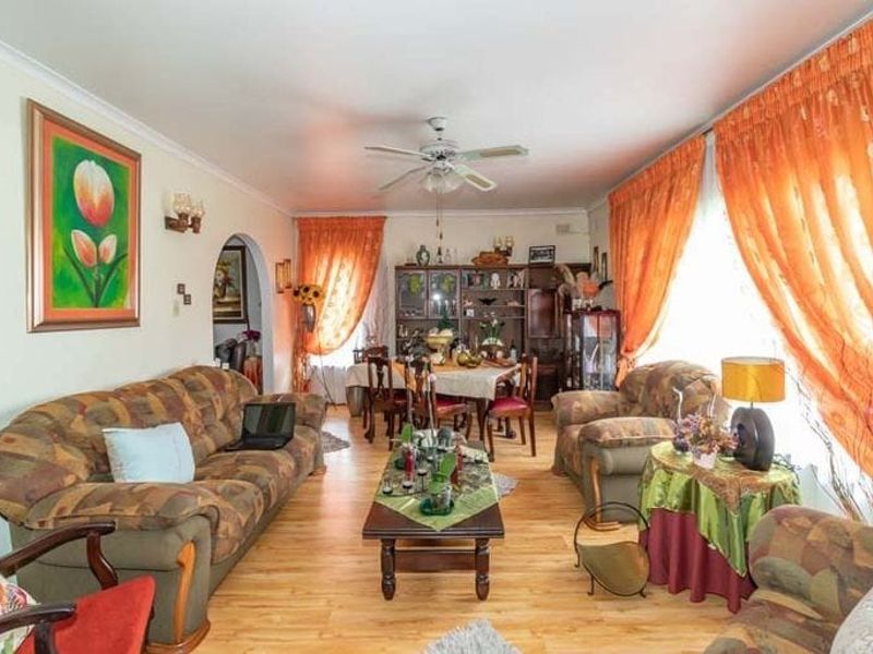 An open-plan living and dining area featuring laminate flooring, a ceiling fan, and an arched entryway leading to adjacent spaces.