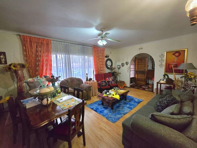 Open plan living and dining area featuring laminate flooring, a ceiling fan, and an arched entryway leading to the home's entrance.