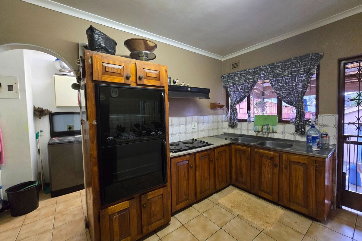 A functional kitchen featuring wooden cabinetry, built-in oven, hob, extractor fan, and a double sink with tiled flooring and backsplash.