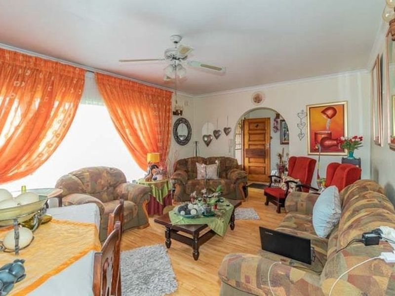 A living room featuring laminate flooring, a ceiling fan, and an arched doorway leading to the entrance.