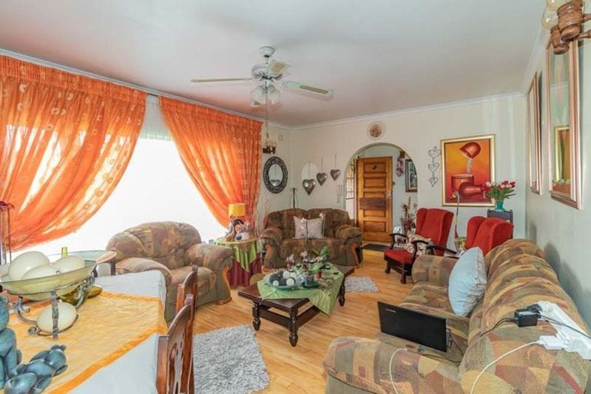 A living room featuring laminate flooring, a ceiling fan, and an arched doorway leading to the entrance.