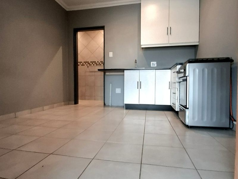 A compact, empty kitchen featuring white cabinetry, tiled flooring, and a freestanding stove, with an adjacent tiled utility area.