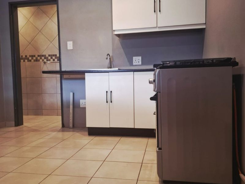 A compact kitchen featuring white cabinetry, tiled flooring, and a neutral grey wall finish, providing a functional and clean preparation space.
