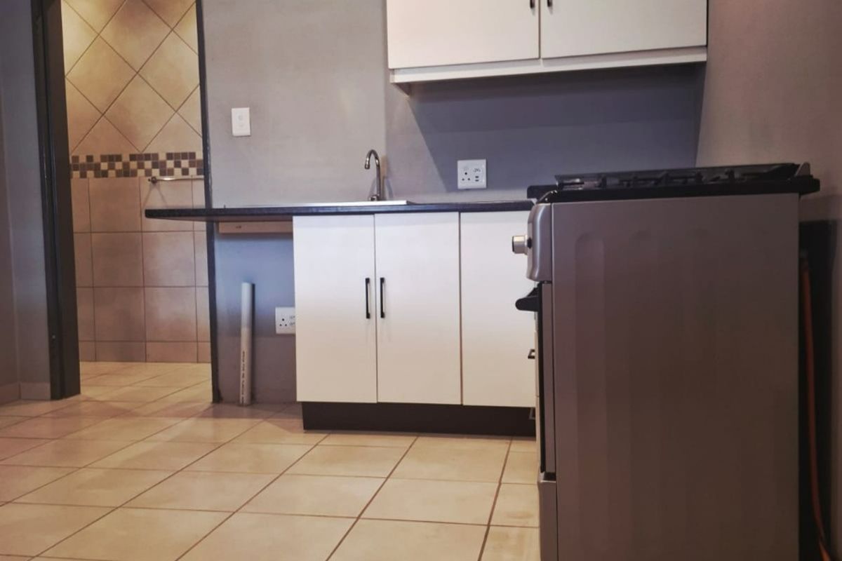 A compact kitchen featuring white cabinetry, tiled flooring, and a neutral grey wall finish, providing a functional and clean preparation space.