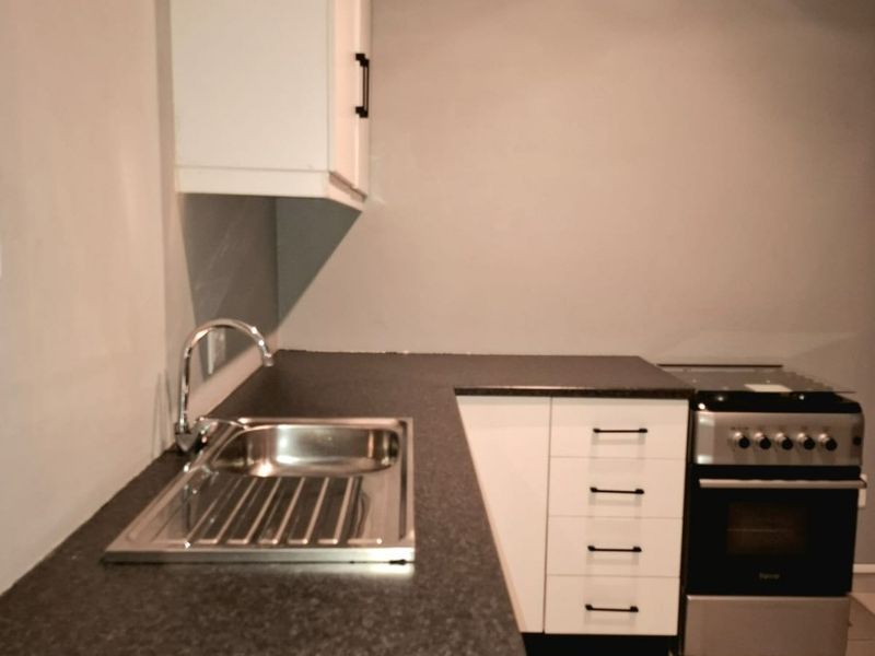 A compact kitchen featuring white cabinetry, dark laminate countertops, a stainless steel sink, and a freestanding stove with tiled flooring.