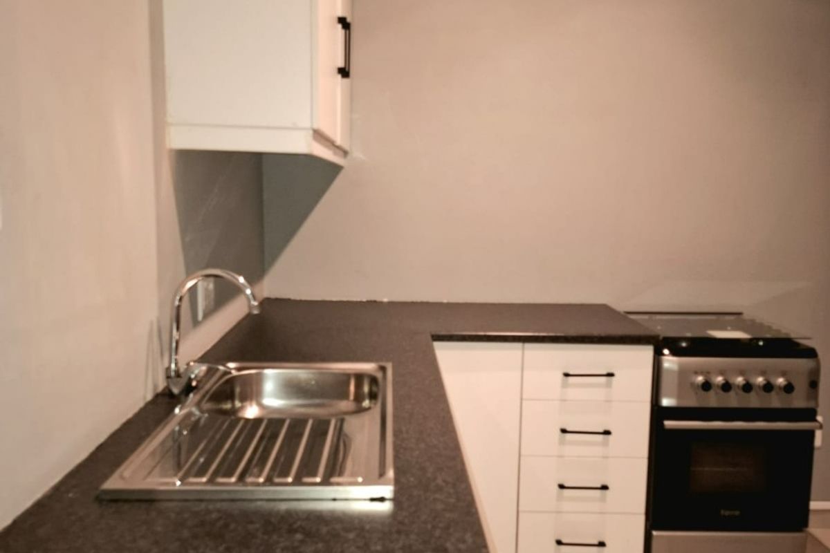 A compact kitchen featuring white cabinetry, dark laminate countertops, a stainless steel sink, and a freestanding stove with tiled flooring.